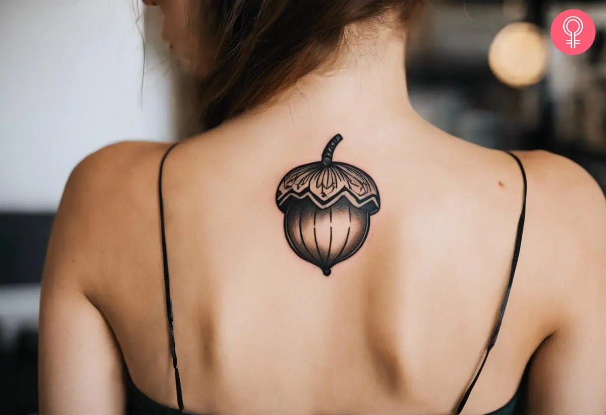 A traditional acorn tattoo on the upper back of a woman