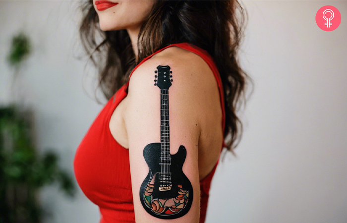 Traditional punk tattoo of a guitar on a woman’s upper arm