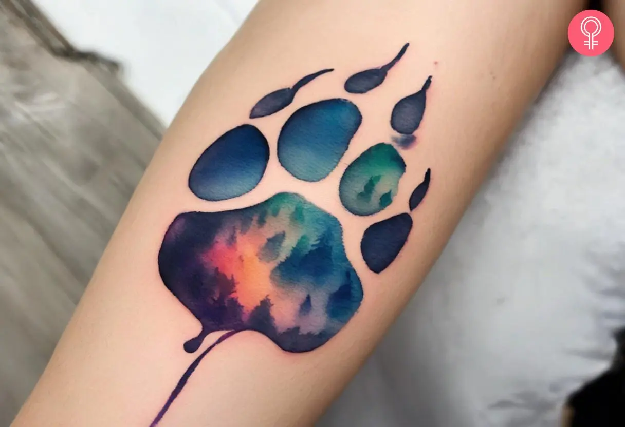 A watercolor wolf paw print tattoo on the arm of a woman