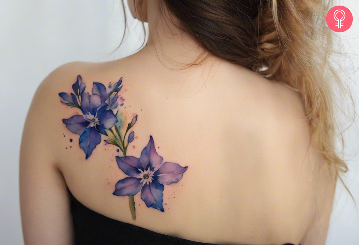 Watercolor larkspur tattoo on a woman’s back