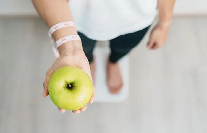 Woman holding an apple checking her weight