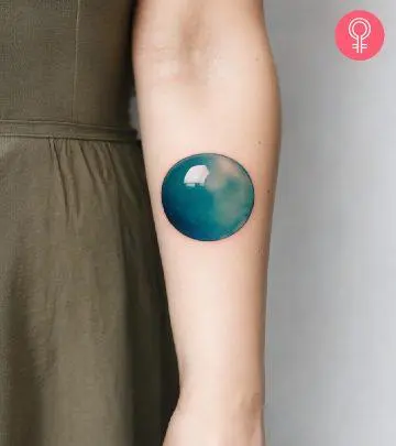 A woman wearing a minimalist fork tattoo on the upper arm.