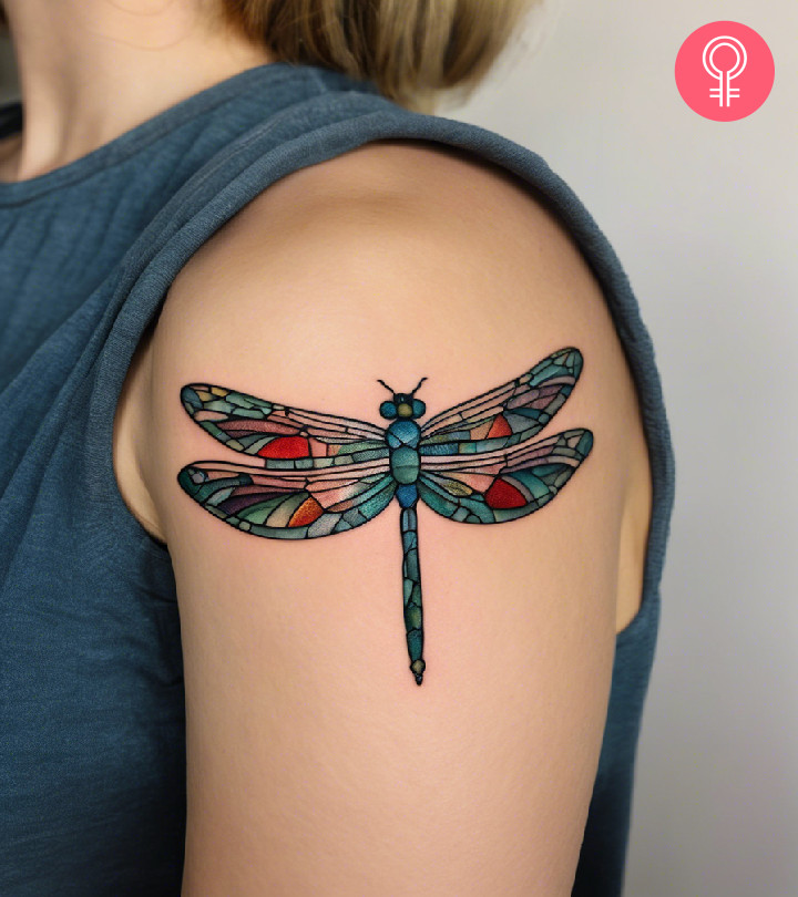 A stained glass patterned dragonfly tattoo on the upper arm