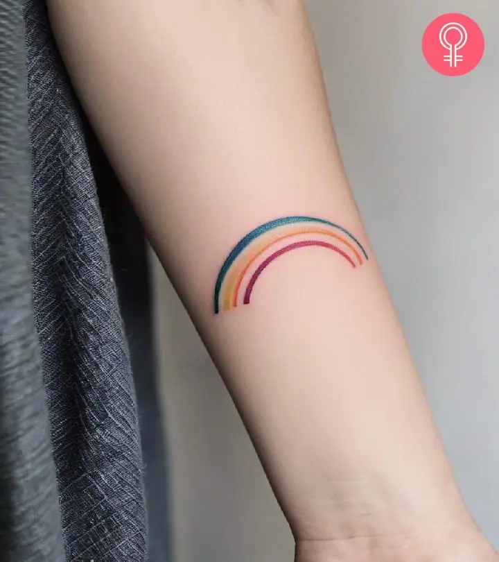 A minimalist rainbow tattoo on the forearm