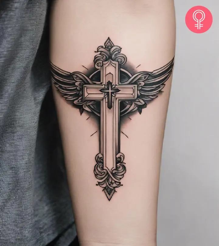 A black and gray cross tattoo with wings inked on the forearm