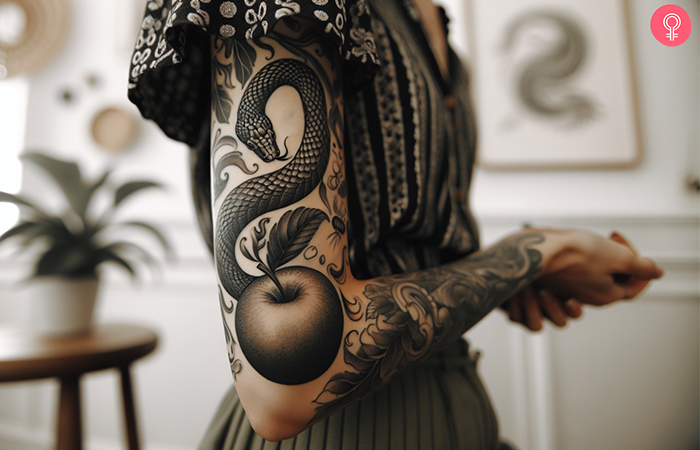 A black ink serpent and apple tattoo on the upper arm