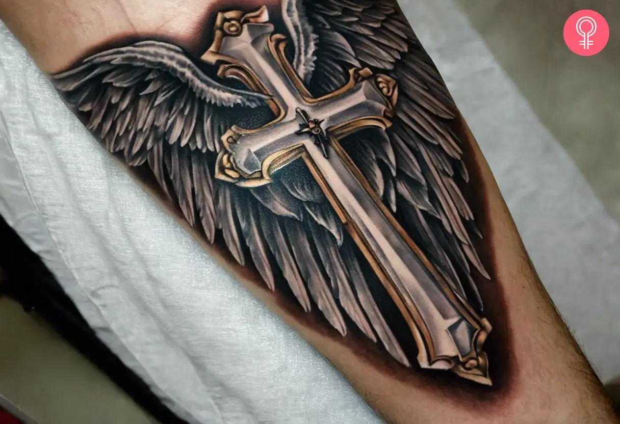 A realistic cross tattoo with wings inked on a man’s forearm