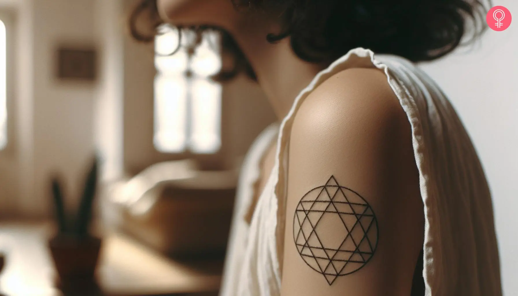 A small minimalist merkaba tattoo on the upper arm of a woman