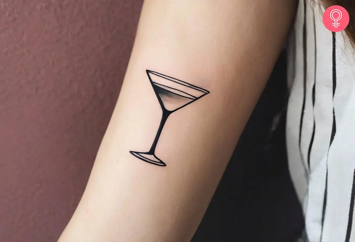 A tiny martini tattoo on the forearm inked in black.