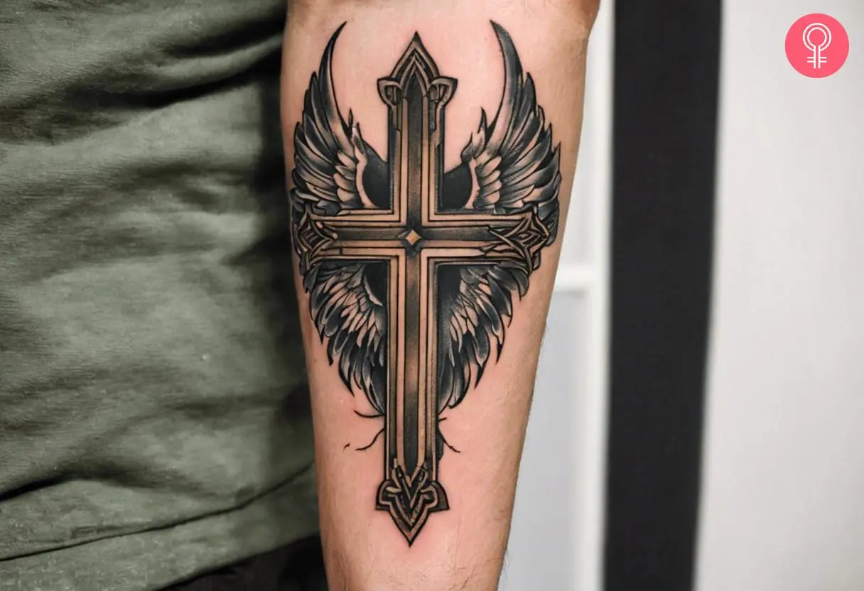 A traditional cross tattoo with wings inked on the forearm