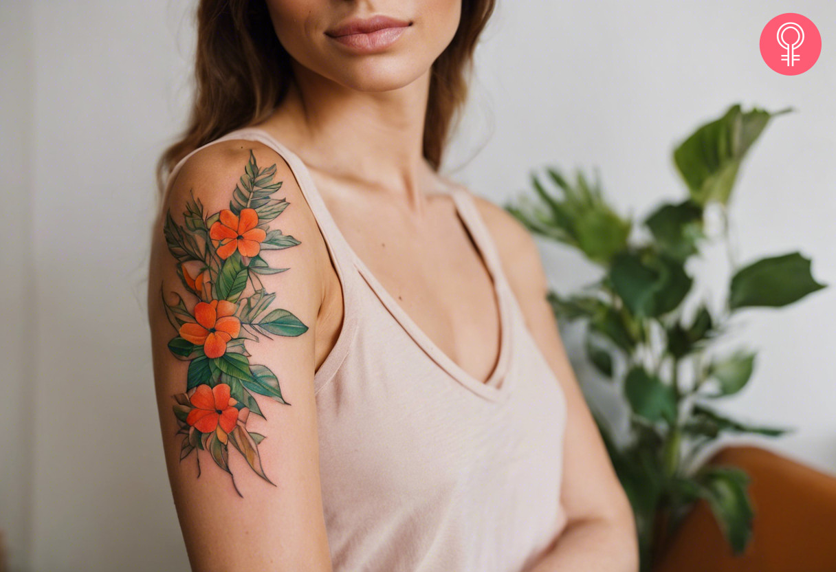 A vibrant foliage tattoo with small orange flowers on a woman’s upper arm