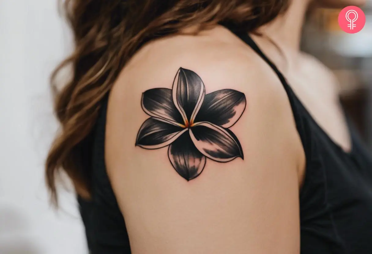 A woman with a black frangipani flower tattoo on her upper arm