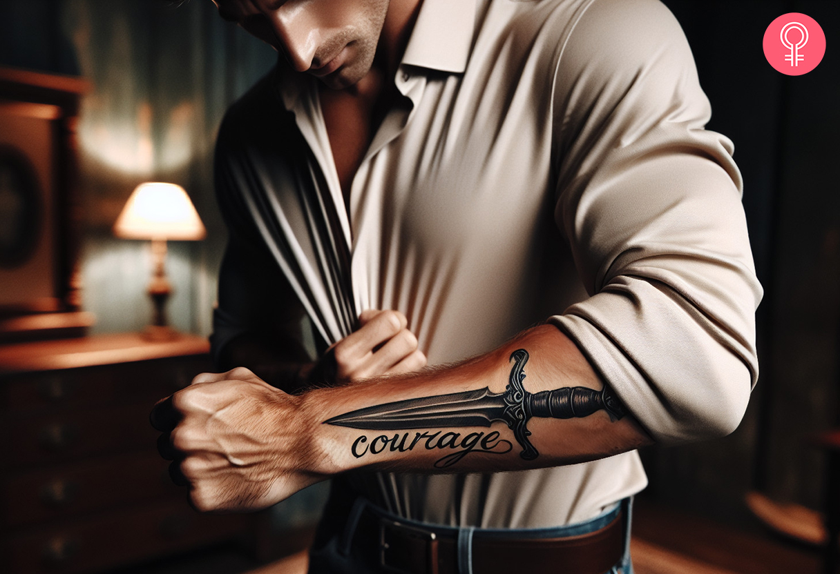 A black and grey courage script tattoo with a dagger on the forearm