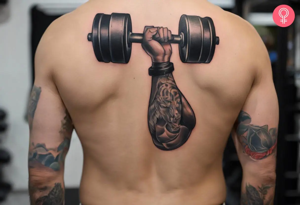 A hand holding a dumbbell tattoo on the back