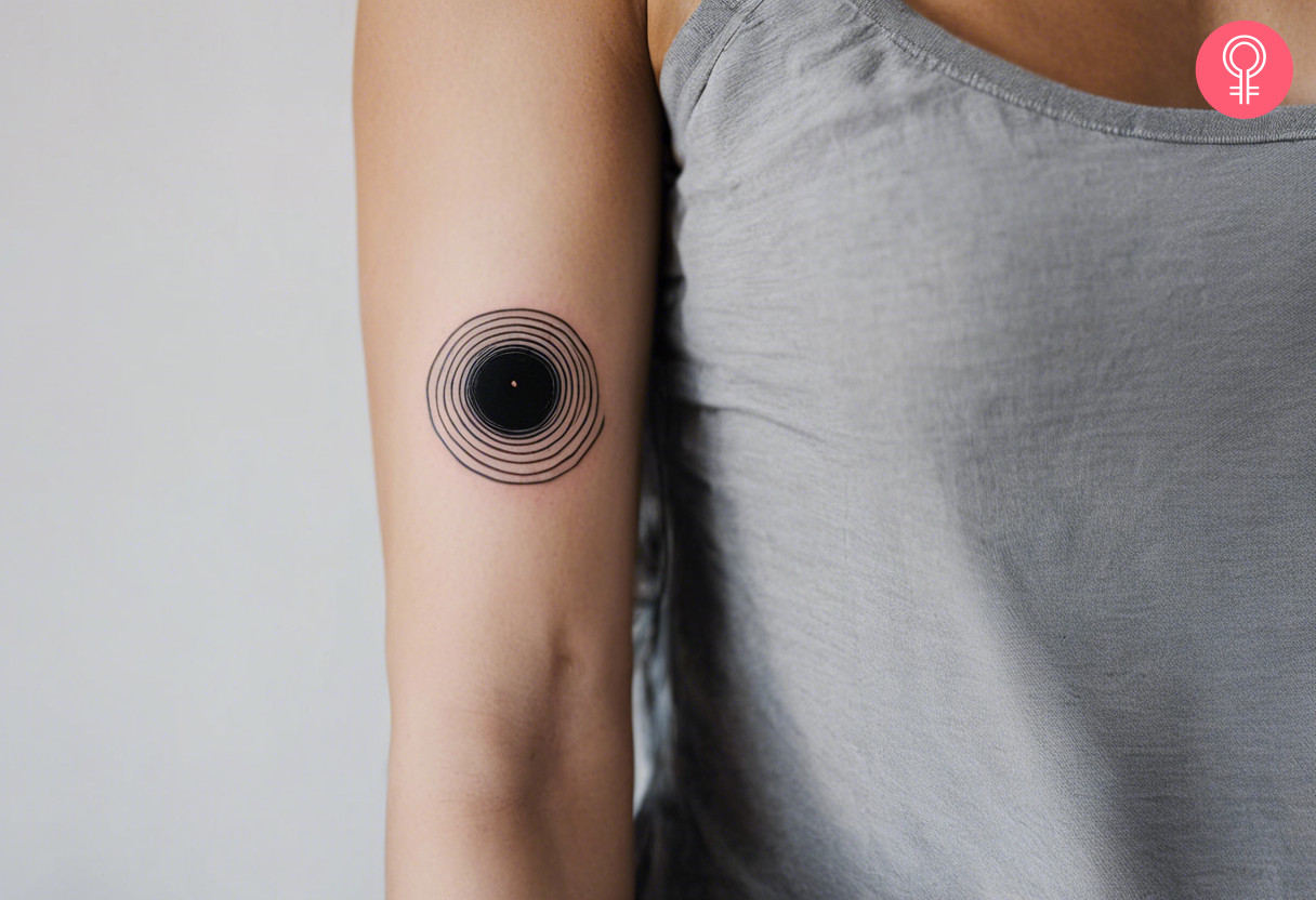 A woman with a minimalist black hole tattoo on her upper arm