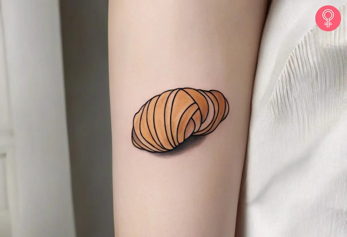 Woman with minimalist croissant tattoo on her outer arm