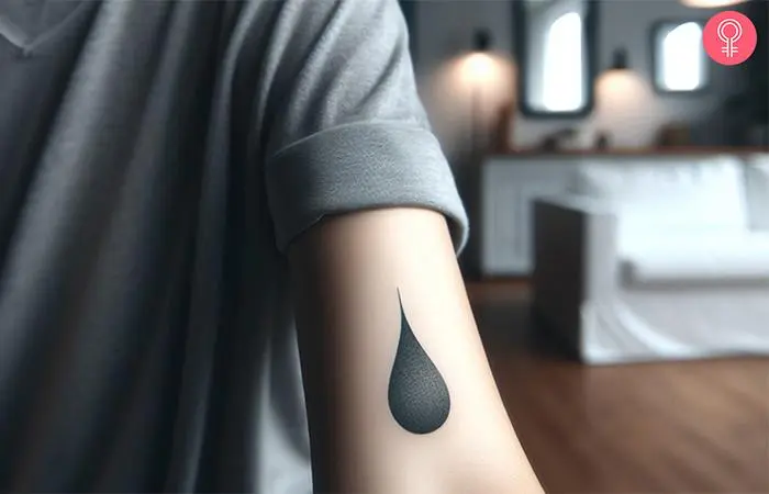 A woman with a minimalist black water drop tattoo on her arm