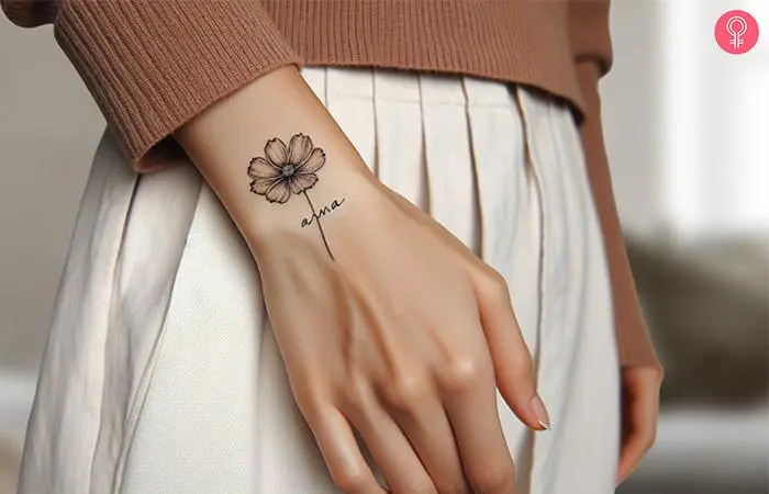 A minimalist cosmos flower with a name inked on the forearm