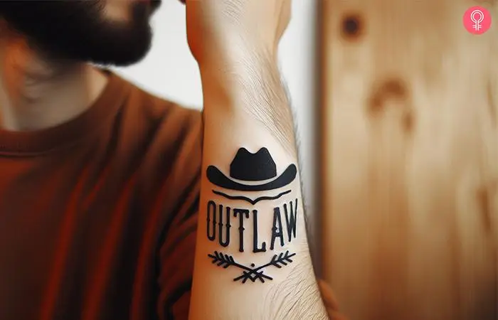 An outlaw text tattoo with a cowboy hat on the wrist