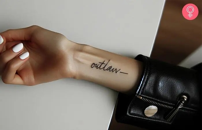 An outlaw cursive text tattoo on the wrist