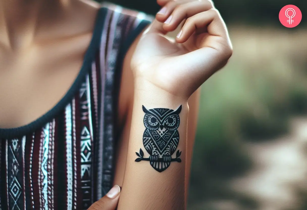 A woman with a small tribal owl tattoo with bold lines and a branch