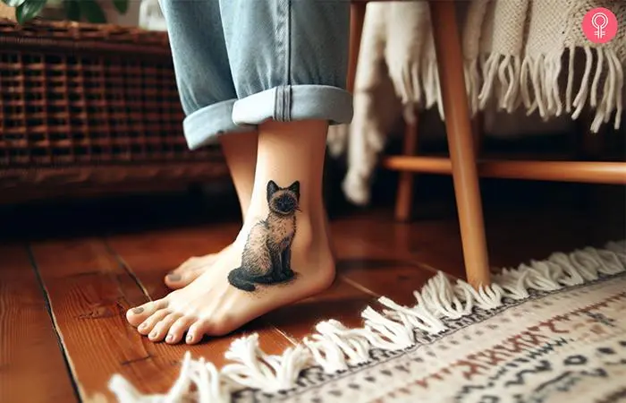 A woman with a minimalist Siamese cat tattoo around the ankle in sitting pose