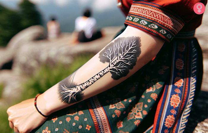 A woman with a black and white birch tree tattoo with negative space for leaves on her arm