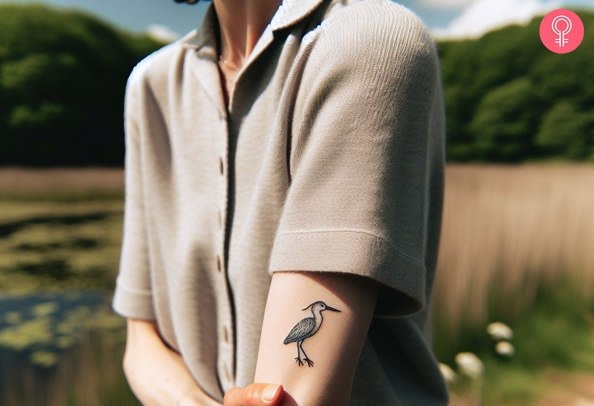 A woman with a minimalist tattoo of a blue heron above the elbow