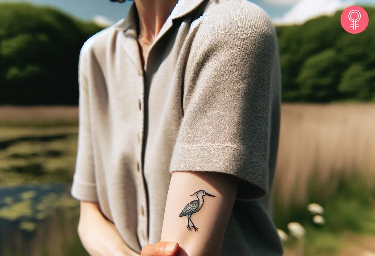 A woman with a minimalist tattoo of a blue heron above the elbow